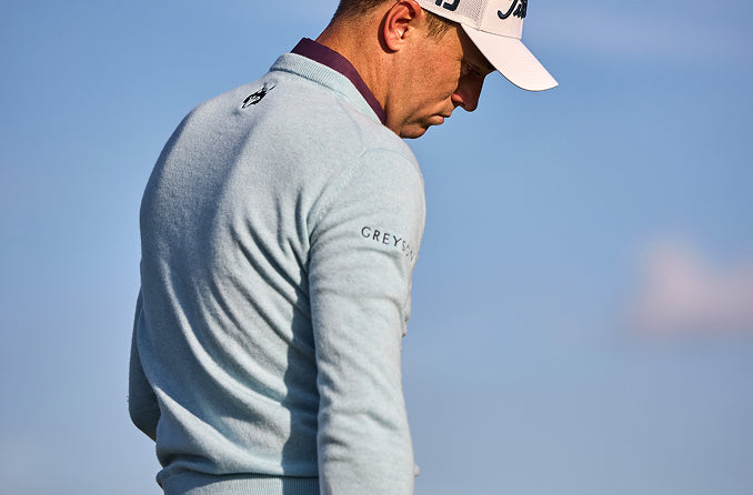 a man on a golf course in a light blue sweater and white hat